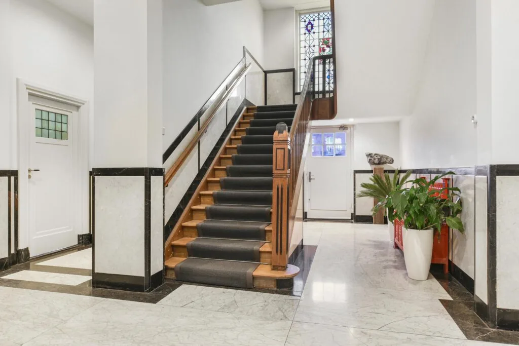 Luxe entreehal aan de Kleine Houtweg met marmeren vloer, houten trap en glas-in-loodraam.